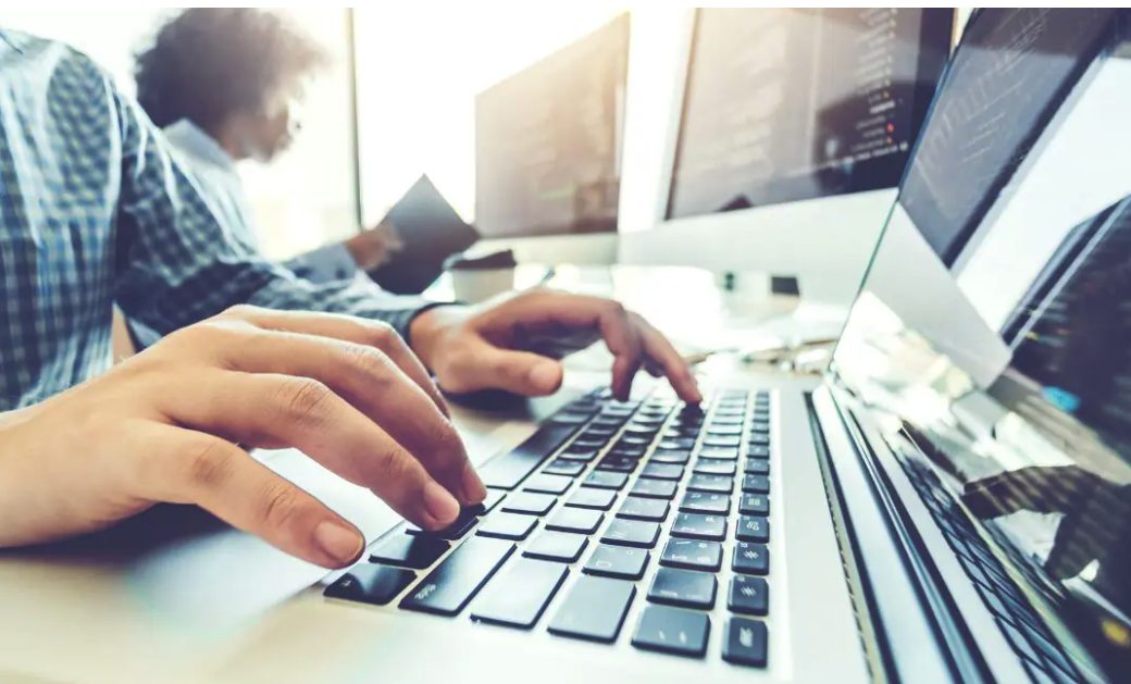 Programmatori al lavoro su codice davanti a più schermi