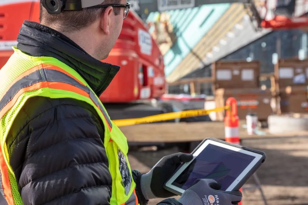 Operatore in cantiere con tablet davanti a una piattaforma aerea